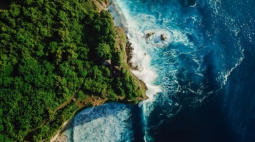 Aerial down view of coastline with rocky cliffs, ocean with waves and lighthouse in Bali